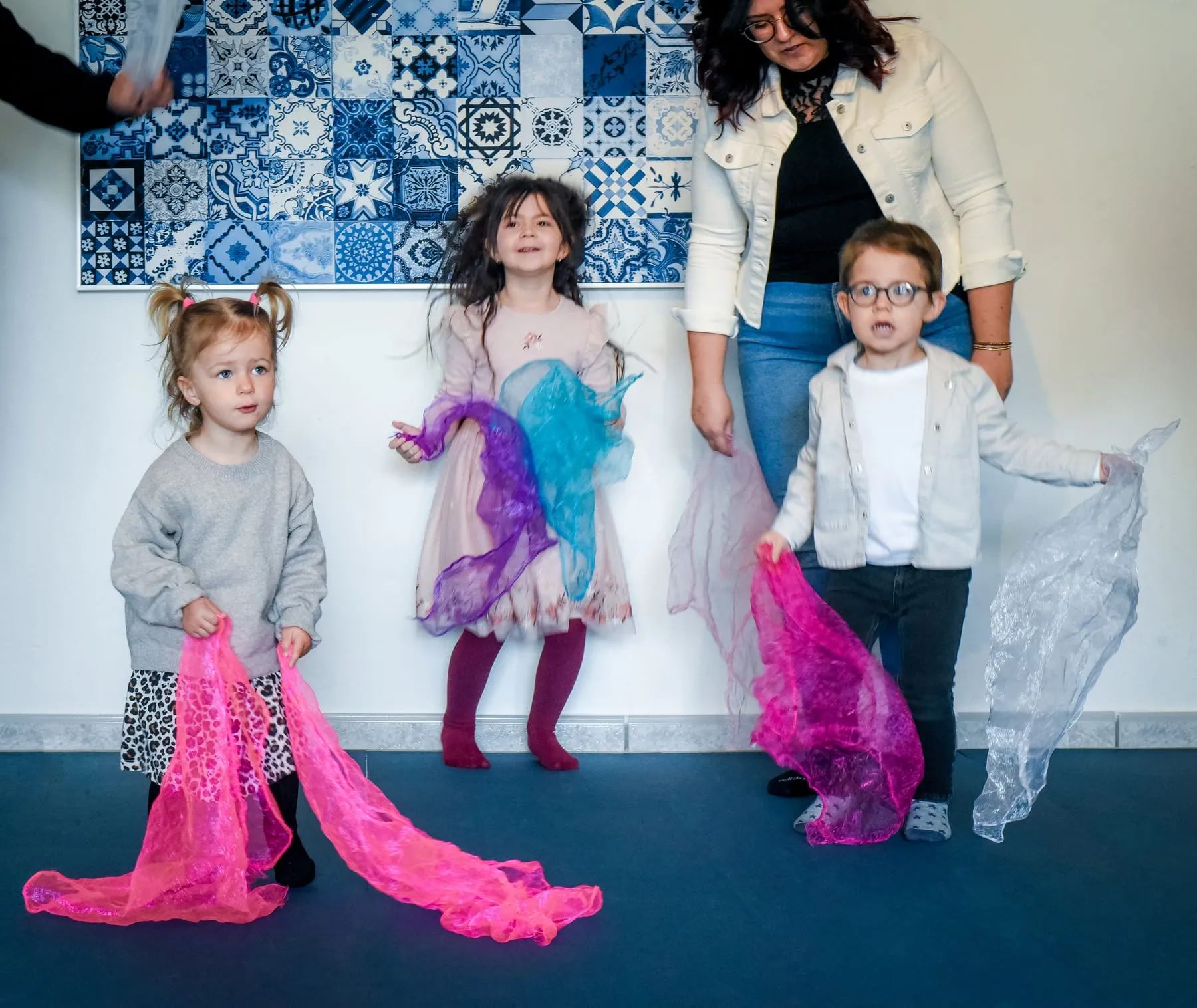 Drei Kinder schwingen bunte Tücher, hinter ihnen steht eine Frau, die auch ein Tuch hält