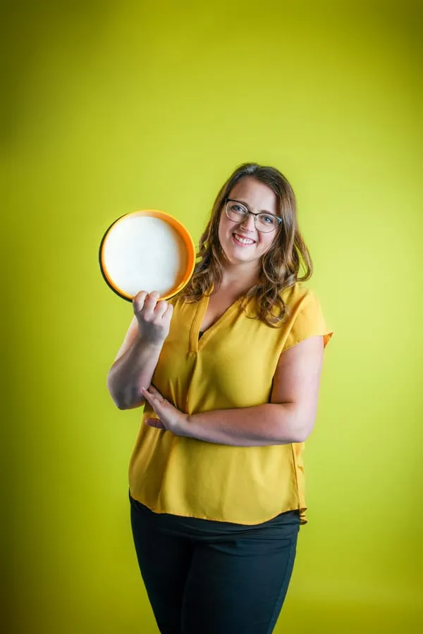 Porträt von Kathi, sie hält eine orangefarbene Handtrommel hoch